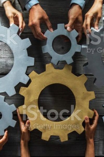 Group of business people joining together silver and golden colored gears on table at workplace top view